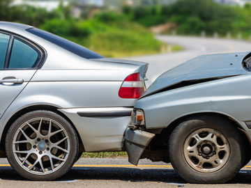 Zwei Autos sind auf einer Straße in einen Auffahrunfall verwickelt; ein silbernes Auto mit sichtbaren Schäden am Heck und ein graues Auto, dessen Front stark eingedrückt ist.