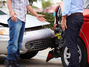 Zwei Männer besprechen den Schaden nach einem Autounfall und stehen neben einem verbeulten roten Auto und einem verknitterten silbernen Fahrzeug.